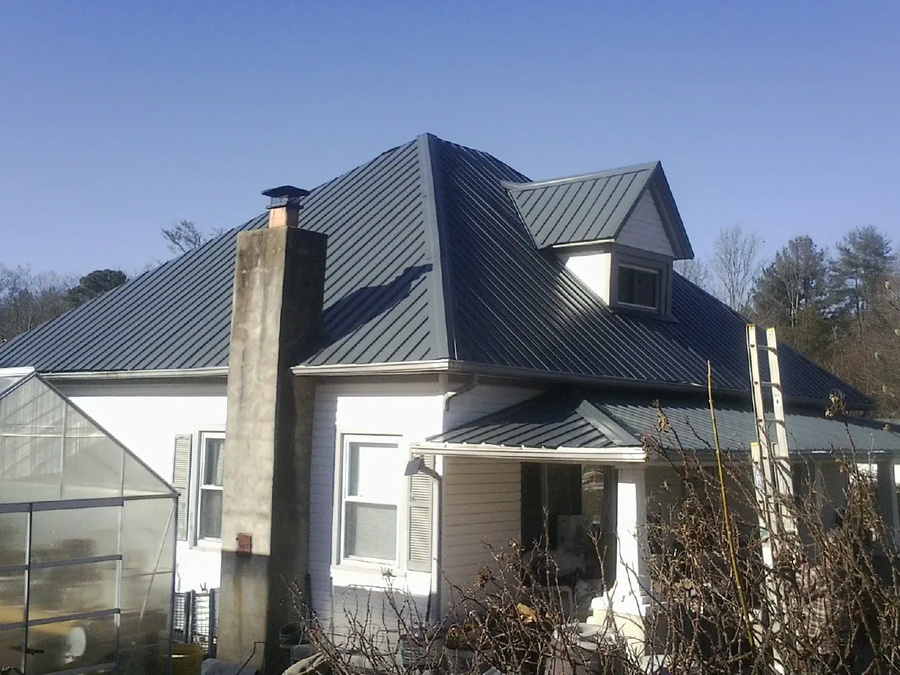 Dark blue standing seam metal roof on a white farmhouse with dormer — Slate & Tile Roof Repair by Roofing Brothers in New Enterprise