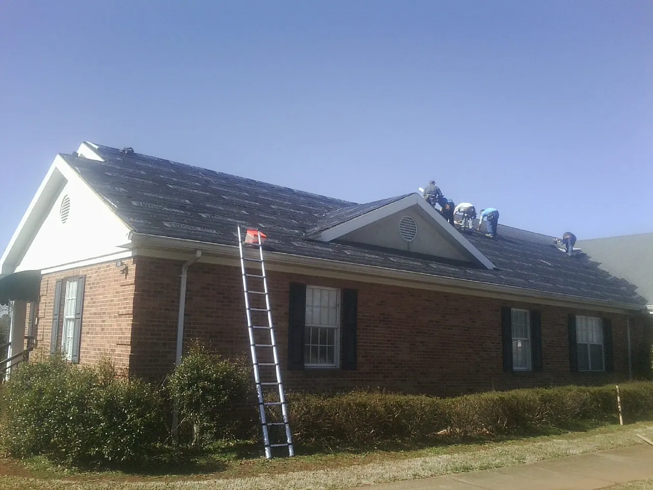 Crew tearing shingles off a brick ranch roof with a ladder set — Emergency Roof Repair work by our crew in New Enterprise