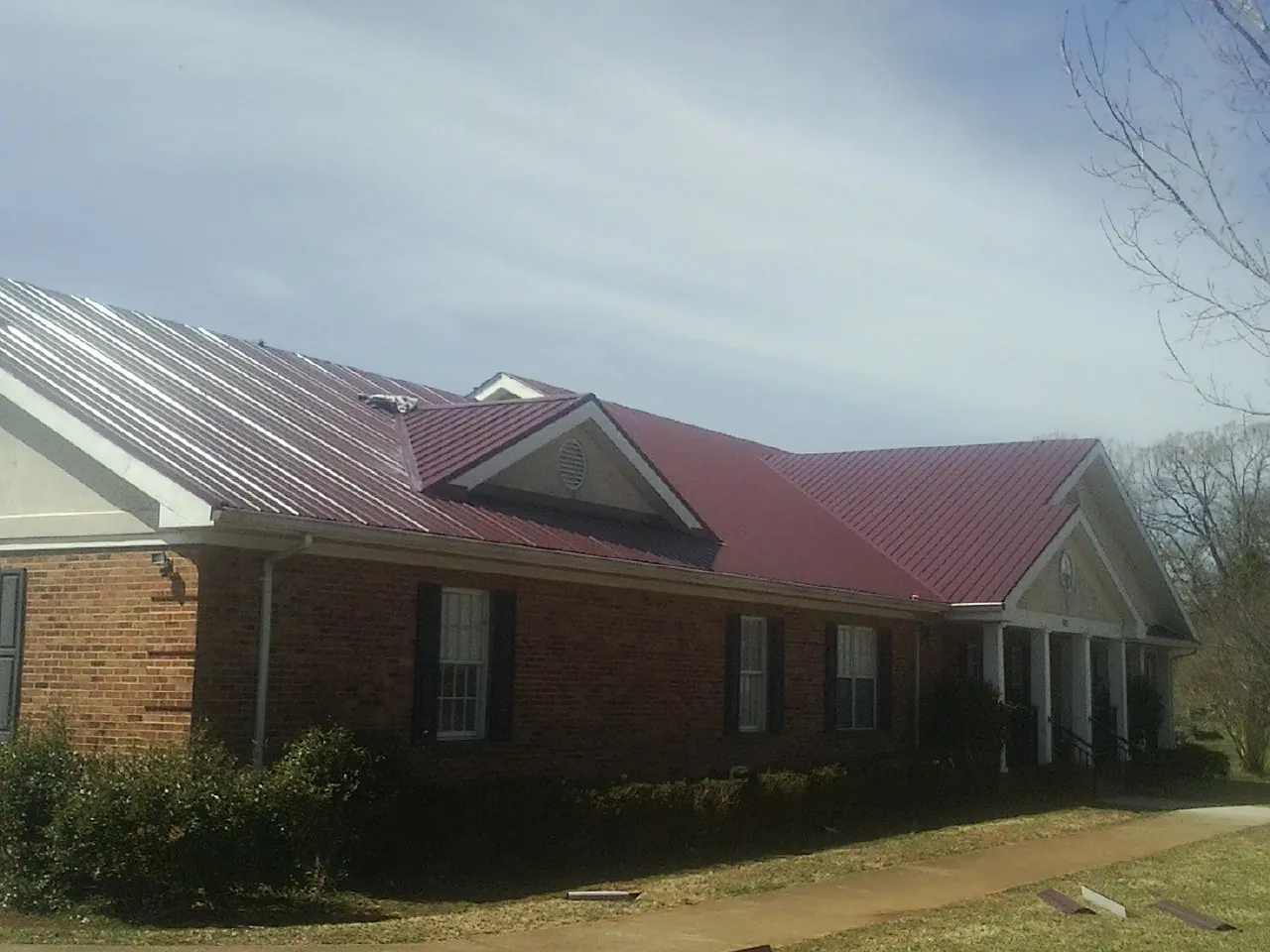 Red metal roof with gabled entries on a long brick building, from a Hail Damage Roof Repair job in New Enterprise