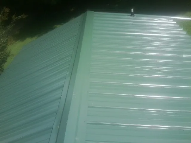 New green metal panels meeting at the ridge of a roof — Flat Roof Repair work by our crew in New Enterprise