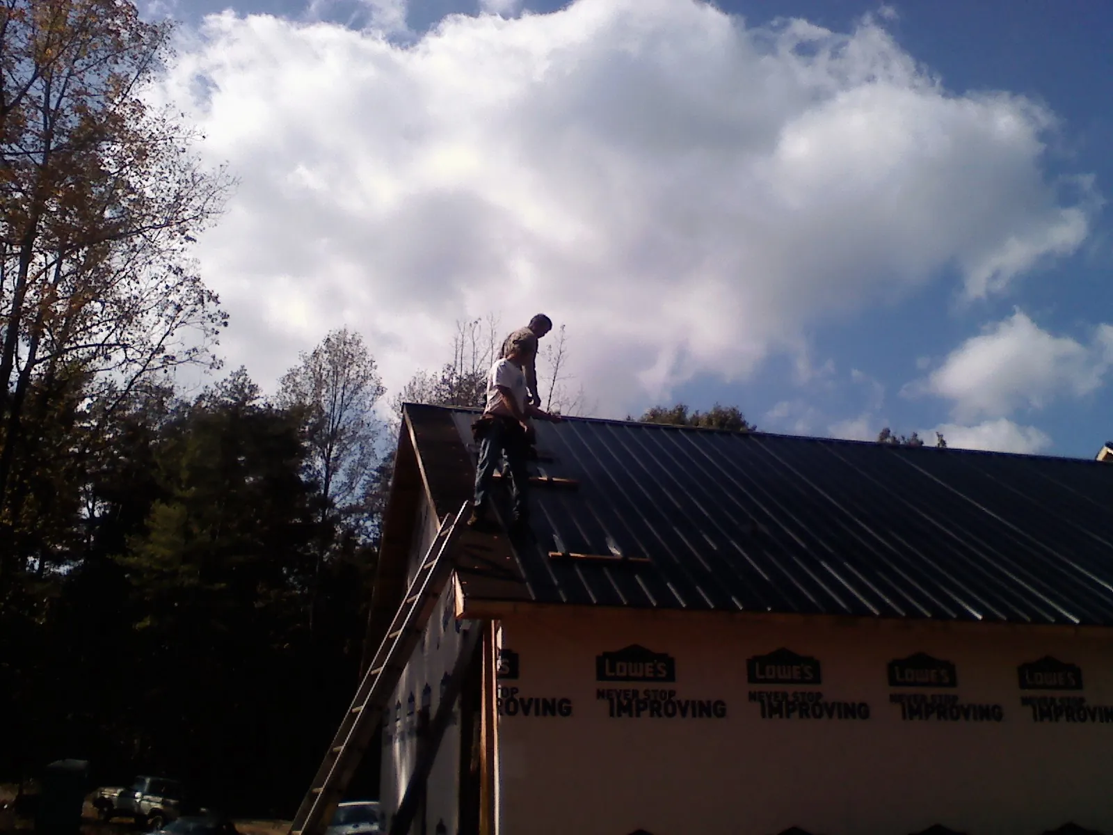 Roofer fastening dark metal panels high against a cloudy sky, from a Roof Inspection job in New Enterprise