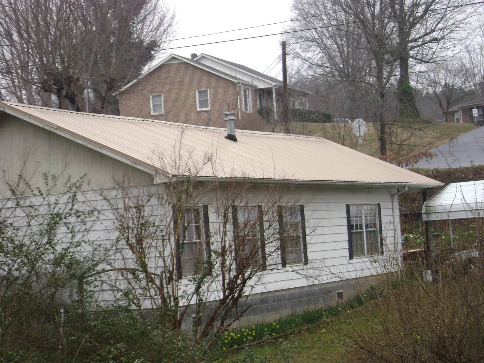 Tan metal roof on a white sided house set into a hillside — Commercial Roofing by Roofing Brothers in New Enterprise